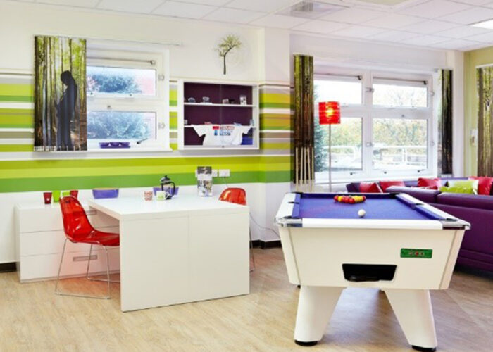 Teenage Cancer Trust social zone decorated in purple and green with striped wall art, pool table, table and chairs and sofas.