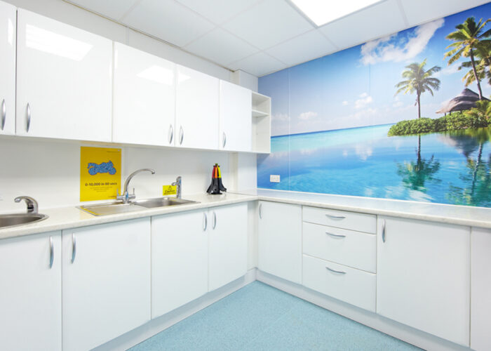 White hospital kitchen with a wall mural showing palm trees and the blue sky reflecting in the water.