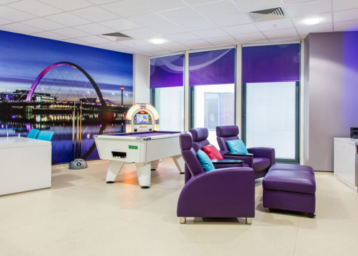 Teenage Cancer Trust hospital room containing pool table with purple cloth, purple chairs, wall art depicting London scene with purple colours and table with co-ordinating turquoise chairs.